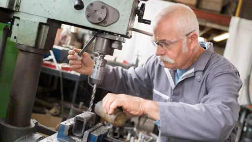 senior metal worker using industrial drilling machine in workshop