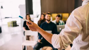 Formateur sur la droite se tenant debout, et de dos, devant quelques personnes attentives