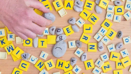Pions avec des lettres dessus, type Scrabble, blancs et jaunes, petits galets avec des lettres &eacute;crites dessus, tous m&eacute;lang&eacute;s, main sur la gauche saisissant un pion