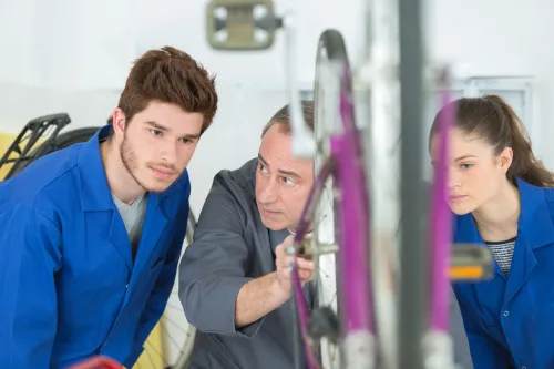 Jeunes en bleu de travail, en formation, avec un professeur, en train de r&eacute;parer un deux-roues